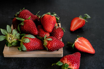 fresh and colorful strawberries on a board, one of them is cut in half. They are on a black background