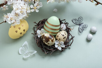 Easter eegs in the nest with flowers and butterfly on pastel green background