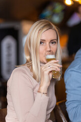Young cheerful blond woman looking at you while toasting with glass of beer