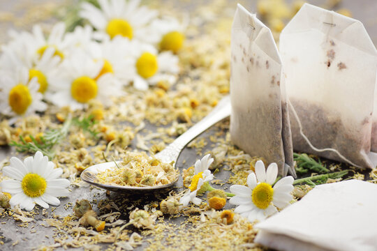 Dried chamomile herbal tea in a spoon with paper tea bags and flowers on black background, closeup, healing drink, natural medicine and naturopathy concept