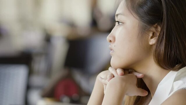 thoughtful young Asian woman waiting for someone sitting in a cafe  