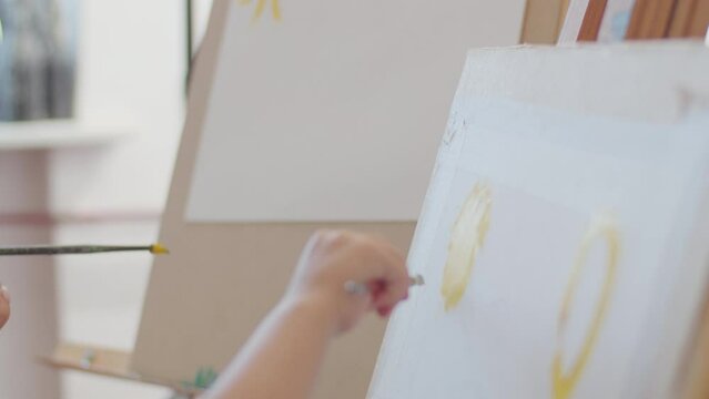 Child painting with yellow color on canvas at art class. Close-up of creativity in action. Artistic development and early education concept. Design for educational content, posters, and workshops