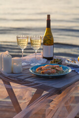 Romantic sunset dinner on the beach. Table honeymoon set for two with luxurious food, glasses of champagne drinks in a restaurant with sea view. Summer love, romance date on vacation concept.