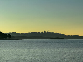 Distant silhouette view of coastal town Vrsar during dramatic sunset, Istria, Croatia. Calm sea surface reflects vibrant colors of sky. Vacation Adriatic Mediterranean Sea in summer. Church on hill