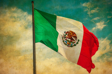 Grunge image of Mexico flag over blue cloudy sky.