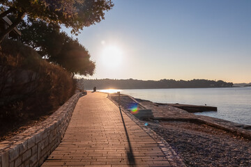 Idyllic promenade walkway along pebble beach of coastal town Funtana during sunset, Istria, Croatia. Calm sea surface and coastline of Adriatic Mediterranean Sea. Seaside vacation concept in summer © Chris