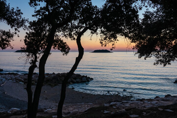 Watching dramatic sunset at coastal village Funtana, Istria, Croatia, EU. Silhouette of remote tropical island. Calm sea surface reflects vibrant colors of sky. Vacation at Adriatic Mediterranean Sea