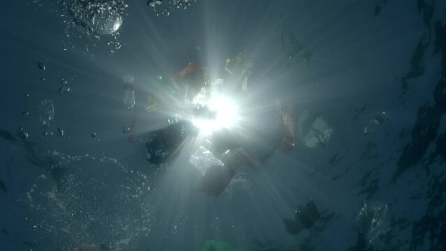 Plastic waste is captured beneath the water&rsquo;s surface in backlight from the sun, casting shadows that underscore the looming issue of underwater pollution.
