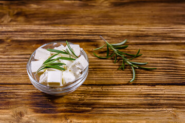 Chopped feta cheese and rosemary in glass bowl on a wooden table