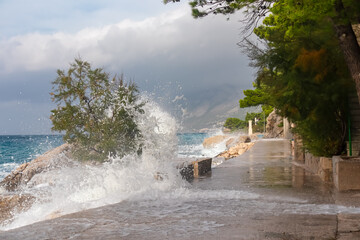 Massive strong waves crashing against coastal walkway in idyllic town Brela, Makarska Riviera in Dalmatia, Croatia. Splashing water spraying mist up into air. Coastline of Adriatic Mediterranean Sea