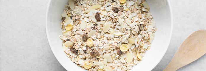 Top view of oat muesli in a white ceramic bowl, overhead view of muesli with oats almonds raisins and cornflakes in a white breakfast bowl, prepping healthy granola breakfast bowl