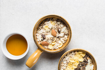 Top view of oat muesli in a brown terracotta ramekin with handle, overhead view of muesli with oats almonds raisins and cornflakes in a brown breakfast bowl, prepping healthy granola breakfast bowl
