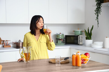 Beautiful Asian woman drinking juice in kitchen