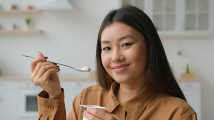 Asian korean woman girl tasting healthy nutrition eat creamy fruit yogurt in kitchen chinese girl...