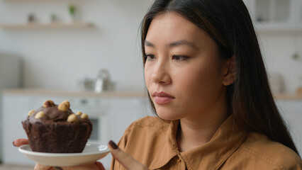 Asian korean woman hungry girl in kitchen hold high-calorie cake deny to eat chocolate dessert keep...