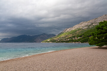 Naklejka premium Idyllic beach Punta Rata with no people in idyllic town Brela, the pearl of Makarska Riviera in Dalmatia, Croatia. Scenic view of majestic coastline of Adriatic Mediterranean Sea on cloudy summer day