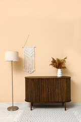 Modern brown chest of drawers, floor lamp and vase with pampas grass near beige wall in room