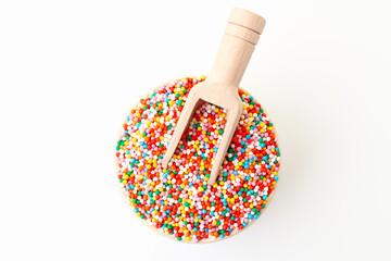 Confectionery sprinkles in bowl with wooden scoop on white background. Decoration for cake and bakery. Top view