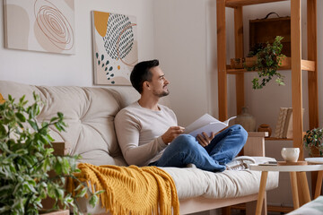Handsome man with magazine resting on white sofa in modern living room