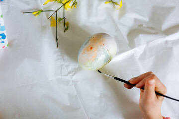 upper view of child hand coloring the easter egg with brush on the table