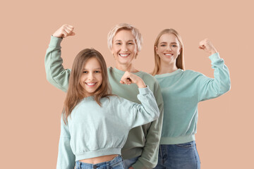 Little girl with her mom and grandmother showing muscles on beige background - obrazy, fototapety, plakaty