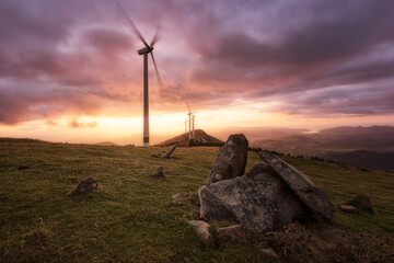 Destroyed dolmen on Mount Oiz, Bizkaia, in the background wind turbines under a warm and dramatic...