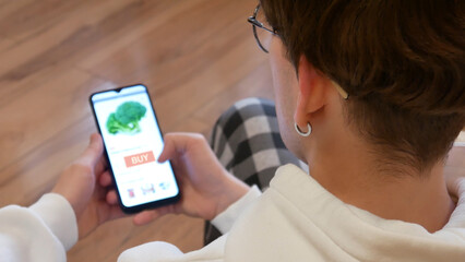 A young man chooses fresh broccoli in an online grocery store
