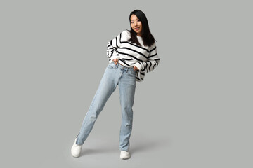 Fototapeta premium Beautiful young happy Asian woman in stylish jeans on grey background