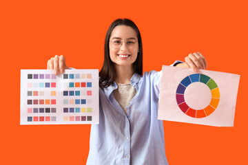 Female designer in eyeglasses with paint color palettes on orange background