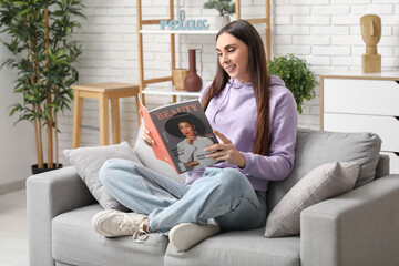Obraz premium Beautiful young woman with magazine sitting on comfortable sofa in living room at home