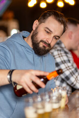 A young handsome man with a beard pouring beer from bottle into glasses