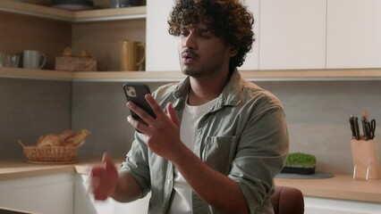 Indian Arabian man at home kitchen playing online game betting cheering favorite sport team with mobile phone unhappy failure upset bad result loose. Male guy with smartphone lost internet connection