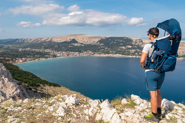 Father with baby carrier on hiking trail with panoramic aerial view of idyllic lagoon in coastal town Baska, Krk Island, Primorje-Gorski Kotar, Croatia, Europe. Coastline of Mediterranean Adriatic Sea