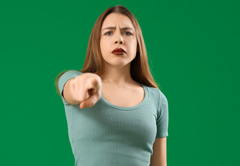 Young woman pointing at viewer on green background. Accusation concept