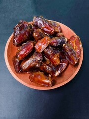 dates on a plate. a pile of dates served on a wooden plate on a black background. sweet brown fruit. healthy meals. food for breaking the fast. Vertical