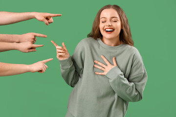 People pointing at laughing young woman on green background. Accusation concept