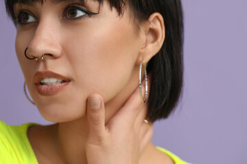 Obraz premium Stylish young woman with nose piercing on lilac background