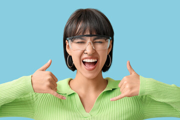 Stylish young woman in eyeglasses with nose piercing on blue background