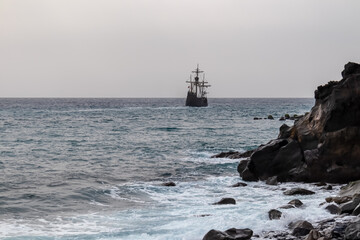 Silhouette of sailing boat ship on the majestic Atlantic Ocean seen from beach Praia Santa Cruz, Madeira island, Portugal, Europe. Sunlight reflection on the calm water surface of the sea. Tranquility