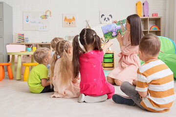 Nursery teacher reading story to little children in kindergarten, back view