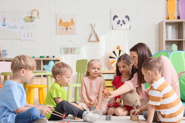 Little children and nursery teacher playing with cubes in kindergarten