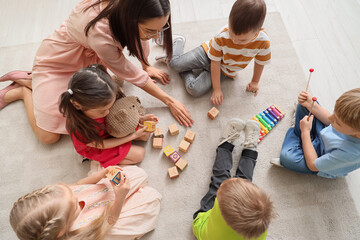 Little children and nursery teacher playing with cubes in kindergarten, top view
