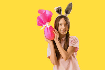 Cute little girl with Easter bunny ears and gift on yellow background
