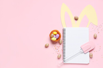 Blank notepad for recipes with Easter decor, colorful sprinkles and spatula on pink background