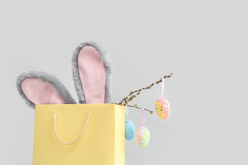 Shopping bag with fluffy bunny ears, pussy willow branches and Easter eggs on white background