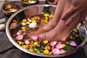 Obraz na płótnie Canvas Foot massage and feet therapy in spa salon in bowl full of pentals of flowers and rose. Pedicure and aromatherapy. Closeup.