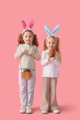 Cute little girls in bunny ears with chocolate Easter eggs on pink background