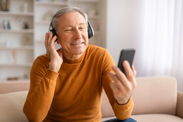 Positive elderly european man using headphones and cell phone