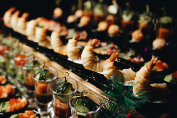 Beautifully decorated catering banquet table with different food snacks and appetizers with sandwich, caviar, fresh fruits on corporate christmas birthday party event or wedding celebration.
