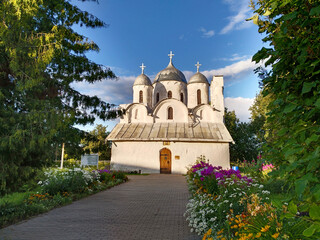Cathedral of Ioann Predtecha (John the Precursor). Church located in Pskov, Russia. Russian temple. Old architecture. Cross. Text Translation: Christ is Risen. Flower bed. - obrazy, fototapety, plakaty